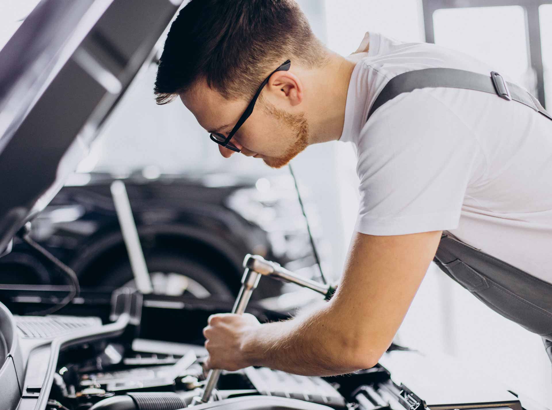 Mechaniker - arbeitet mit Werkzeugen an einem offenen Auto-Motor - in einer Werkstattumgebung.