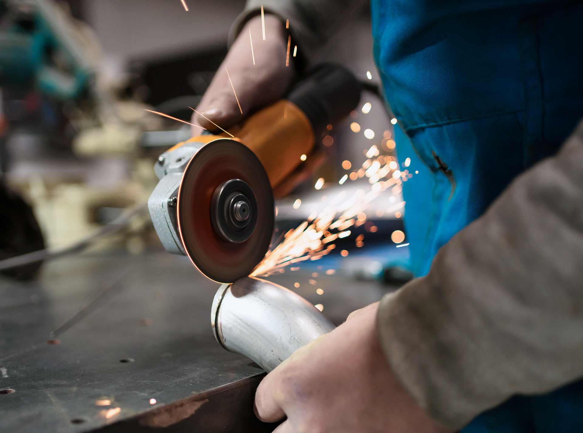 Eine Person schneidet mit einem Winkelschleifer ein Metallrohr, während Funken sprühen, in einer Werkstattumgebung.
