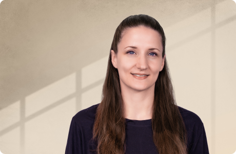 Frau in dunklem Oberteil lächelt leicht vor einem sanft beleuchteten Hintergrund mit geometrischem Schattenmuster. - Anette Ostertag