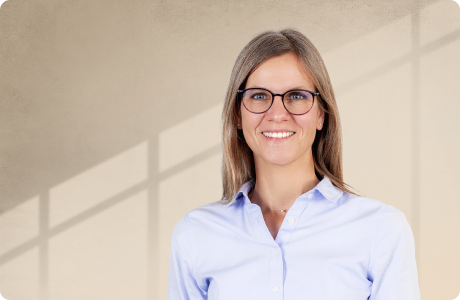 Eine Person mit Brille und blauem Hemd lächelt in die Kamera. Der Hintergrund zeigt Licht und Schatten auf der Wand. - Simone Schindera